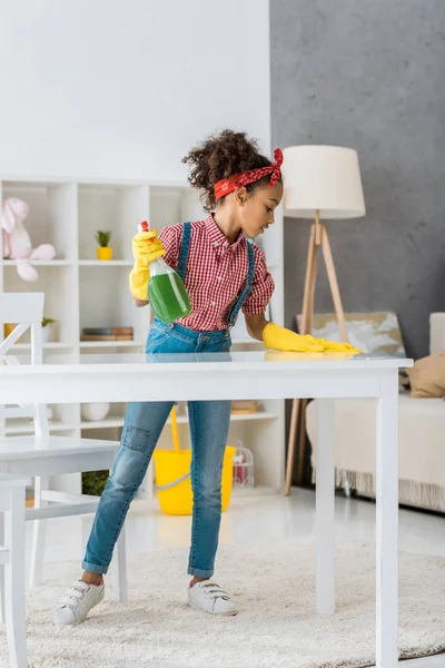 Cute african american child cleaning white table in yellow rubber gloves — Stock Photo