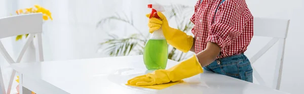 Niño afroamericano con la tabla verde de la limpieza de la botella del aerosol en guantes de goma amarillos - foto de stock