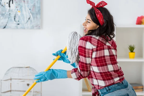 Attractive african american woman in plaid shirt singing with mop — Stock Photo