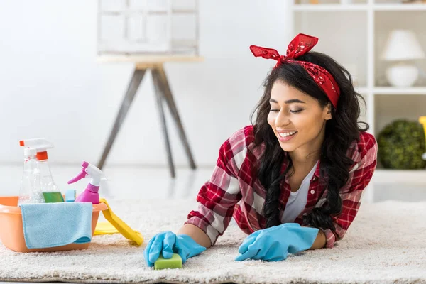 Attraktiver Afroamerikaner liegt auf Teppich und reinigt ihn mit Schwamm — Stockfoto