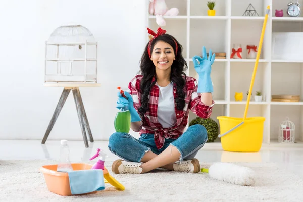 Lächelnde Afroamerikanerin in blauen Gummihandschuhen sitzt in Lotus-Pose und zeigt ok Zeichen — Stockfoto