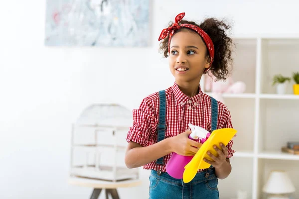 Cute african american girl holding yellow rug and pink spray bottle — Stock Photo