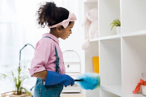 Cute african american chid dusting shelving unit — Stock Photo