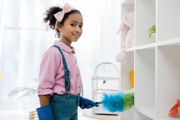 Adorabile africano americano bambino pulizia scaffali con spolverino — Foto stock