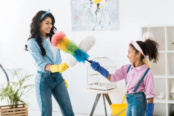 Fröhliche afrikanisch-amerikanische Mutter und Tochter im Kampf mit Staubwedeln — Stockfoto