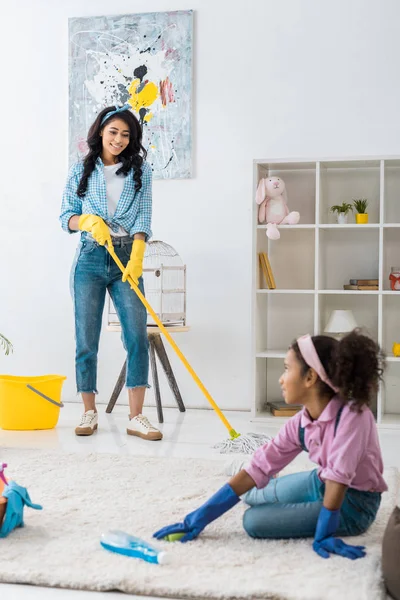 Cute african american child cleaning carpet while mother washing floor — Stock Photo
