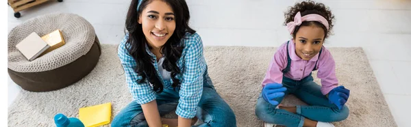 Sonriente africano americano madre y hija sentado en alfombra en loto poses - foto de stock