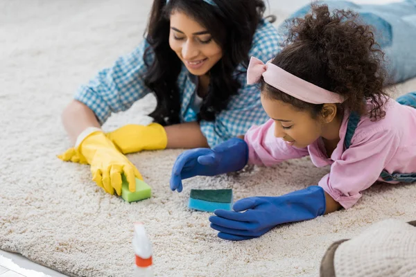 Pretty african american woman with adorable daughter cleaning carpet with sponges — Stock Photo