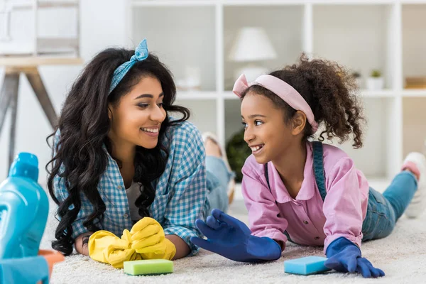 Smiling african american mom and daughter talking while lying on carpet — Stock Photo