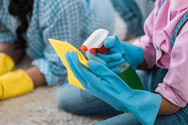 Vista ritagliata del bambino afroamericano spruzzando liquido detergente su uno straccio di gomma giallo — Foto stock