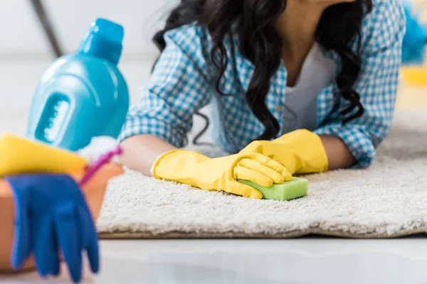 Cropped view of african american woman in yellow rubber gloves lying on carpet with sponge — Stock Photo