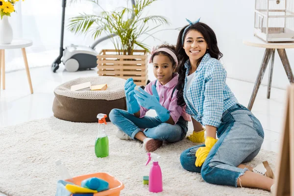 Афро-американських мати і донька одягаються сидячи на килимі з чистячі засоби — стокове фото