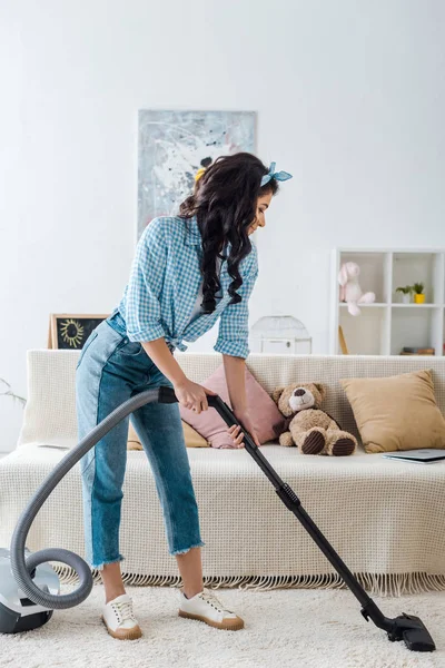 Afrikanische Amerikanerin in kariertem Hemd und blauer Jeans saugt Teppich — Stockfoto