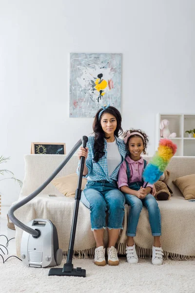 Attractive african american woman sitting on sofa near adorable daughter — Stock Photo