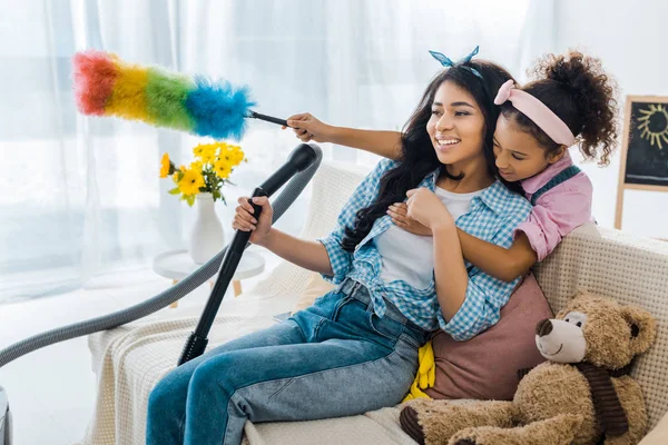 Cute african american child hugging mother from back while holding colorful duster — Stock Photo