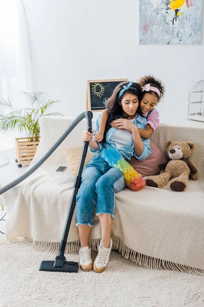 Чарівна афроамериканська дитина обіймає втомлену матір, сидячи на дивані — стокове фото