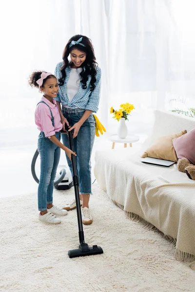 Adorable enfant afro-américain aider la mère à passer l'aspirateur tapis — Photo de stock