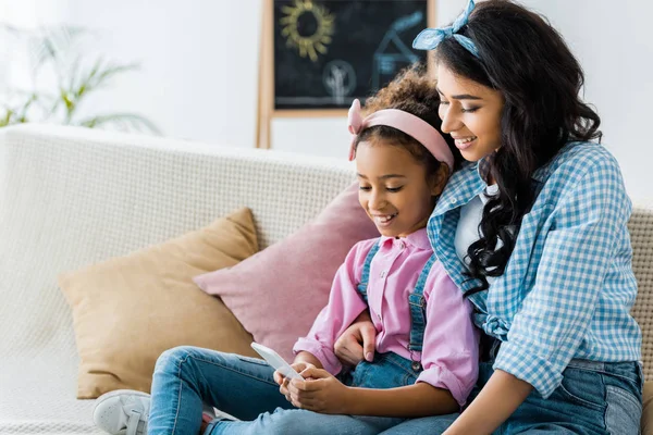 Smiling african american mom with adorable daughter using smartphone together — Stock Photo