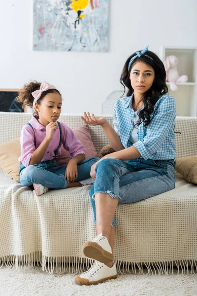 Seria africana americana madre con hija sentado en sofá juntos en casa - foto de stock