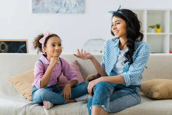 Smiling african american mom and daughter talking while sitting on sofa at home — Stock Photo