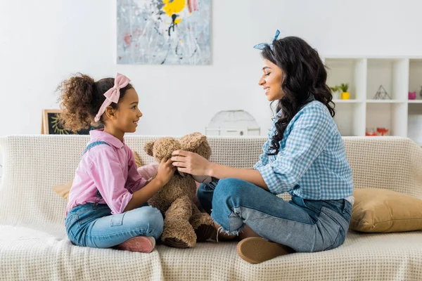 Lindo africano americano niño sentado en sofá con madre en casa - foto de stock