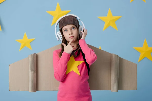 Thoughtful kid in cardboard wings listening music on blue starry background — Stock Photo