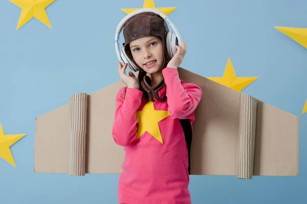 Enfant souriant dans des écouteurs blancs regardant la caméra sur fond bleu avec des étoiles — Photo de stock