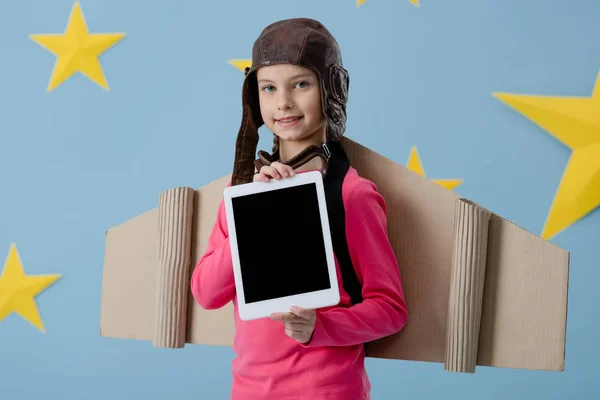 Enfant souriant dans le casque de vol tenant tablette numérique avec écran blanc sur fond bleu étoilé — Photo de stock