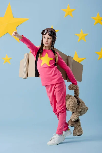 Niño en casco de vuelo divertido posando con oso de peluche sobre fondo azul estrellado - foto de stock