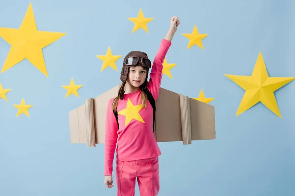 Cute child with cardboard wings holding fits up on blue starry background — Stock Photo