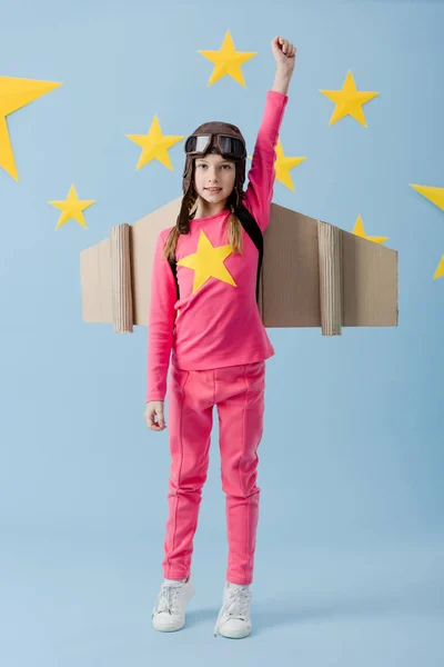 Full length view of kid in flight helmet holding fist up on blue starry background — Stock Photo