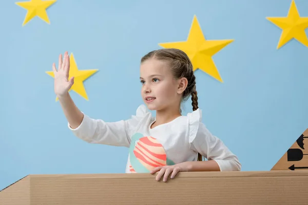 Enfant mignon avec des tresses agitant la main sur fond étoilé bleu — Photo de stock