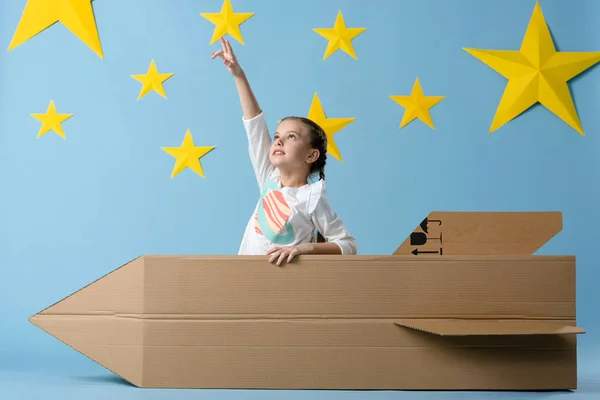 Enfant avec fusée en carton pointant du doigt l'étoile sur fond étoilé bleu — Photo de stock