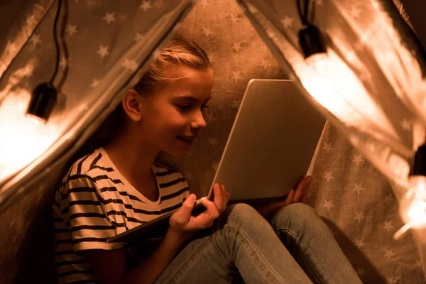 Cheerful kid using laptop in wigwam at home — Stock Photo