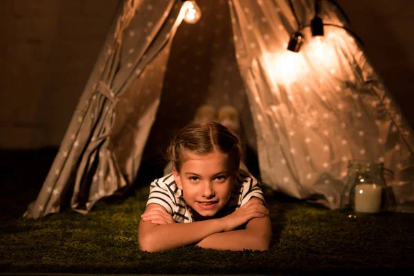 Laughing kid lying on carpet in dark room and looking at camera — Stock Photo