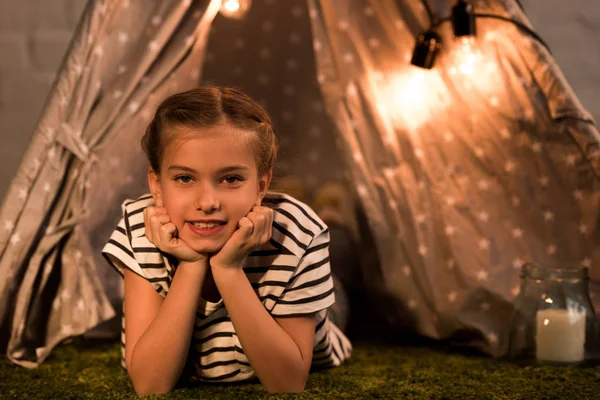 Enfant rêveur couché sur le tapis et regardant la caméra à la maison — Photo de stock