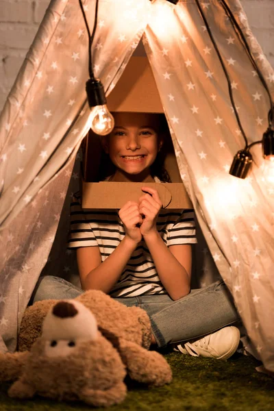 Enfant excité dans un casque en carton assis à Wigwam avec le sourire — Photo de stock