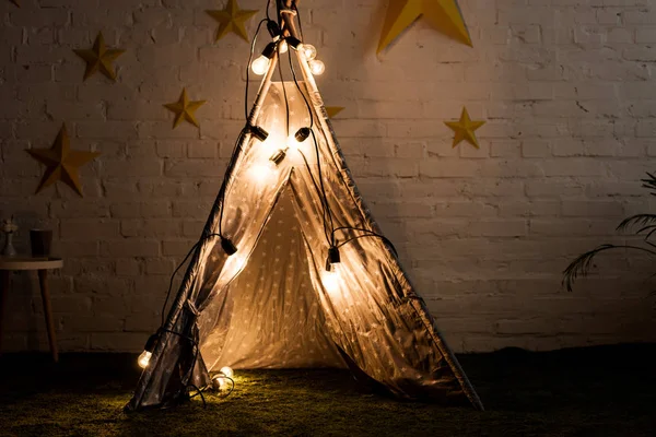 Cozy wigwam with luminous bulbs standing in dak room — Stock Photo