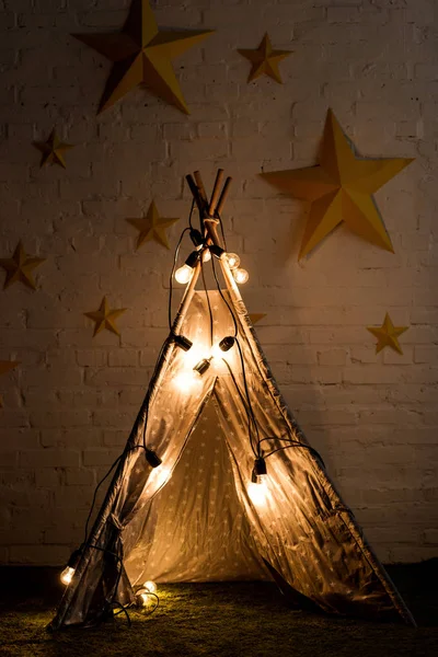 Cozy wigwam with luminous bulbs standing in dark room — Stock Photo
