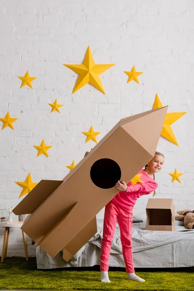 Ansicht des aufgeregten Kindes mit großer Papprakete im Schlafzimmer — Stockfoto