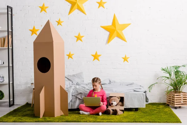 Preteen enfant assis sur le tapis et en utilisant un ordinateur portable dans la chambre — Photo de stock