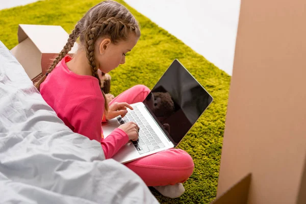 Kid with braids sitting on carpet and typing on laptop keyboard — Stock Photo