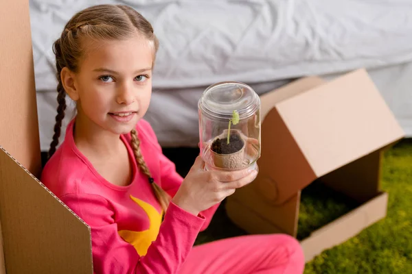 Lindo niño con trenzas sosteniendo la planta en tarro de vidrio - foto de stock