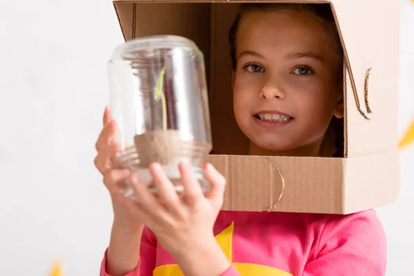 Excited child in cardboard helmet holding plant in jar — Stock Photo