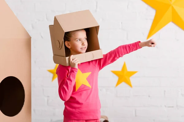 Inspired kid in pink clothes and cardboard helmet holding fist up — Stock Photo