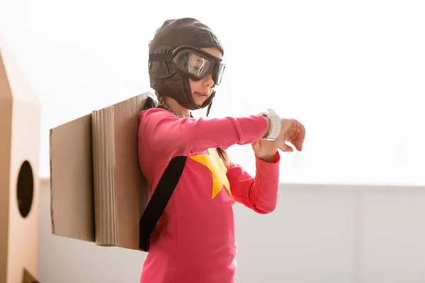 Child in flight helmet and goggles looking at watch — Stock Photo
