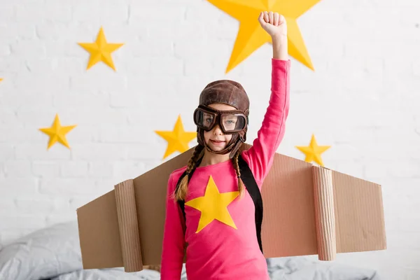 Kid in flight helmet and cardboard wings holding fist up — Stock Photo
