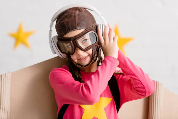 Criança sorridente no capacete de voo e óculos ouvindo música em fones de ouvido — Fotografia de Stock