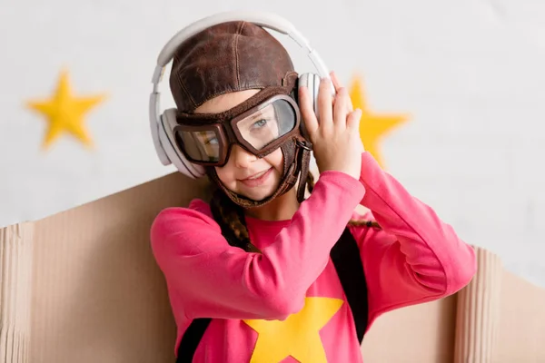 Smiling kid in flight helmet and goggles listening music in headphones — Stock Photo