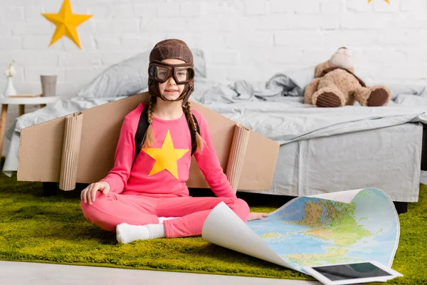 Cute kid in flight helmet sitting on carpet with map — Stock Photo